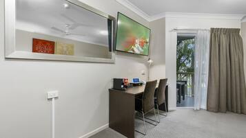 A hotel room with a desk, chairs, a TV, and a view of the outdoors.