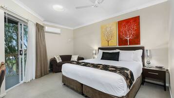 A hotel room with a large bed, a sofa, a ceiling fan, and two paintings on the wall.