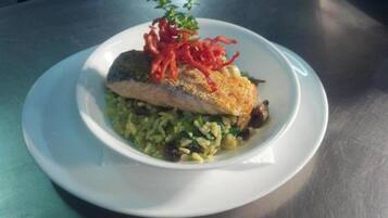 A plate with a piece of fish, rice, and red garnish on a table.