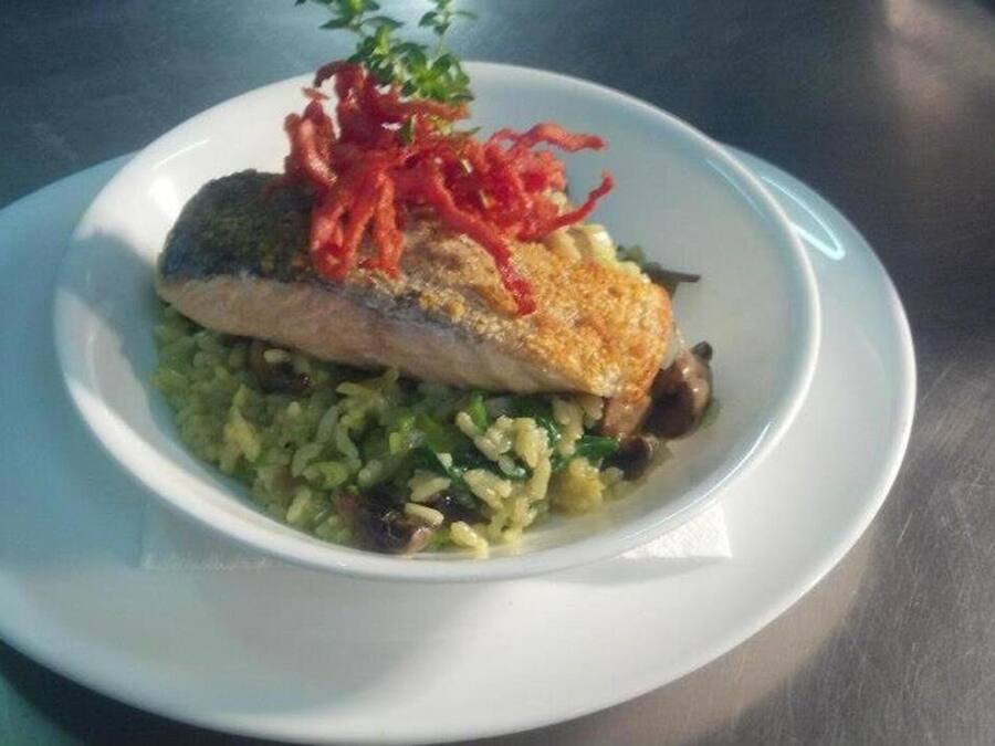 A plate with a piece of fish, rice, and red garnish on a table.