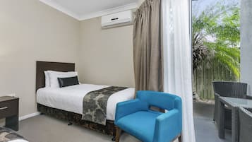 A bedroom with a bed, a blue chair, a small table, and a balcony with a view of greenery.