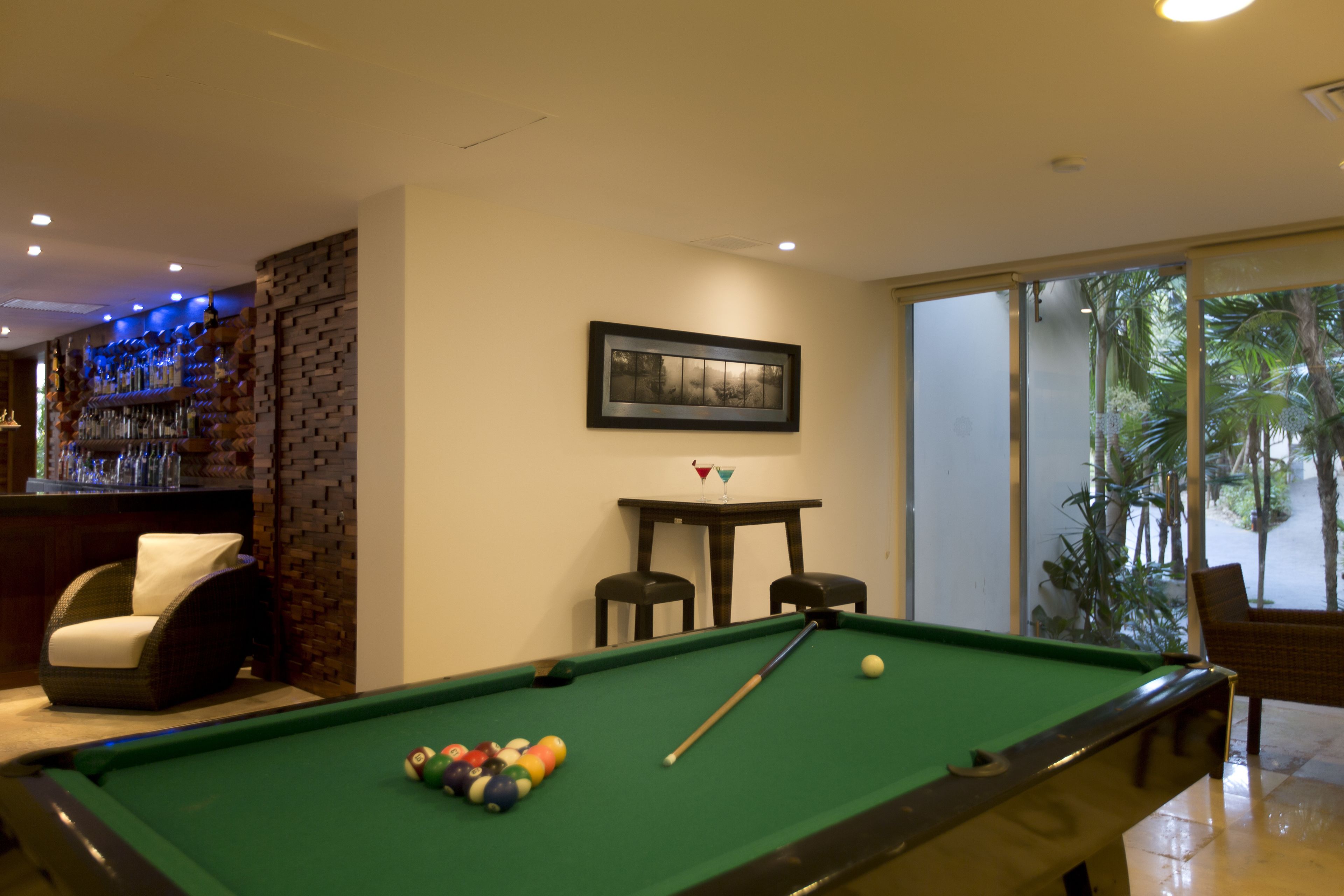 Une table de billard avec des billes, un bar avec des bouteilles et une vue sur des palmiers à travers une porte vitrée.