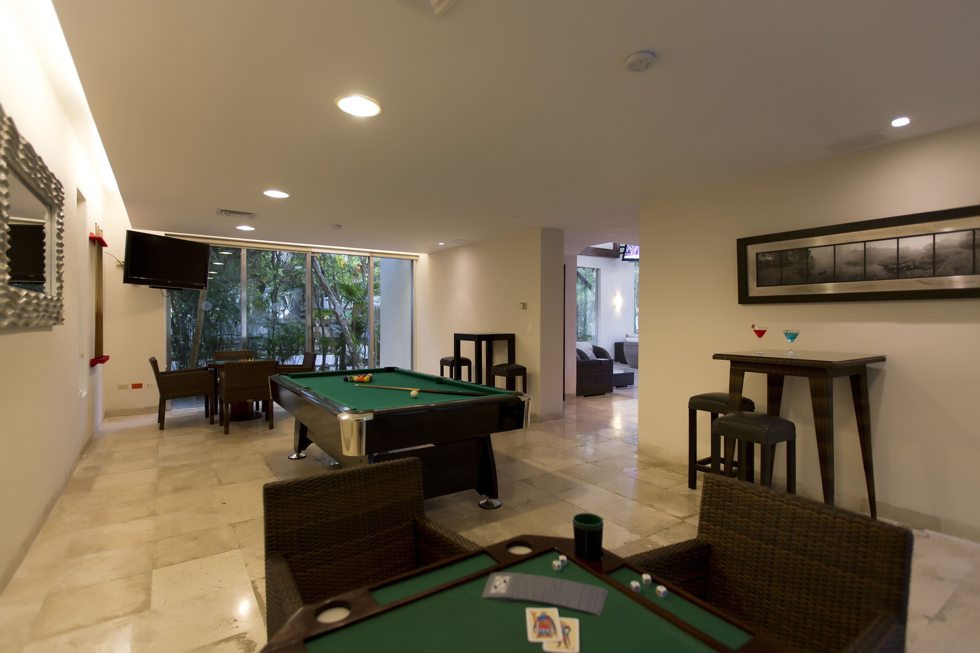 A pool table in a well-lit room with a dining area and a TV on the wall.