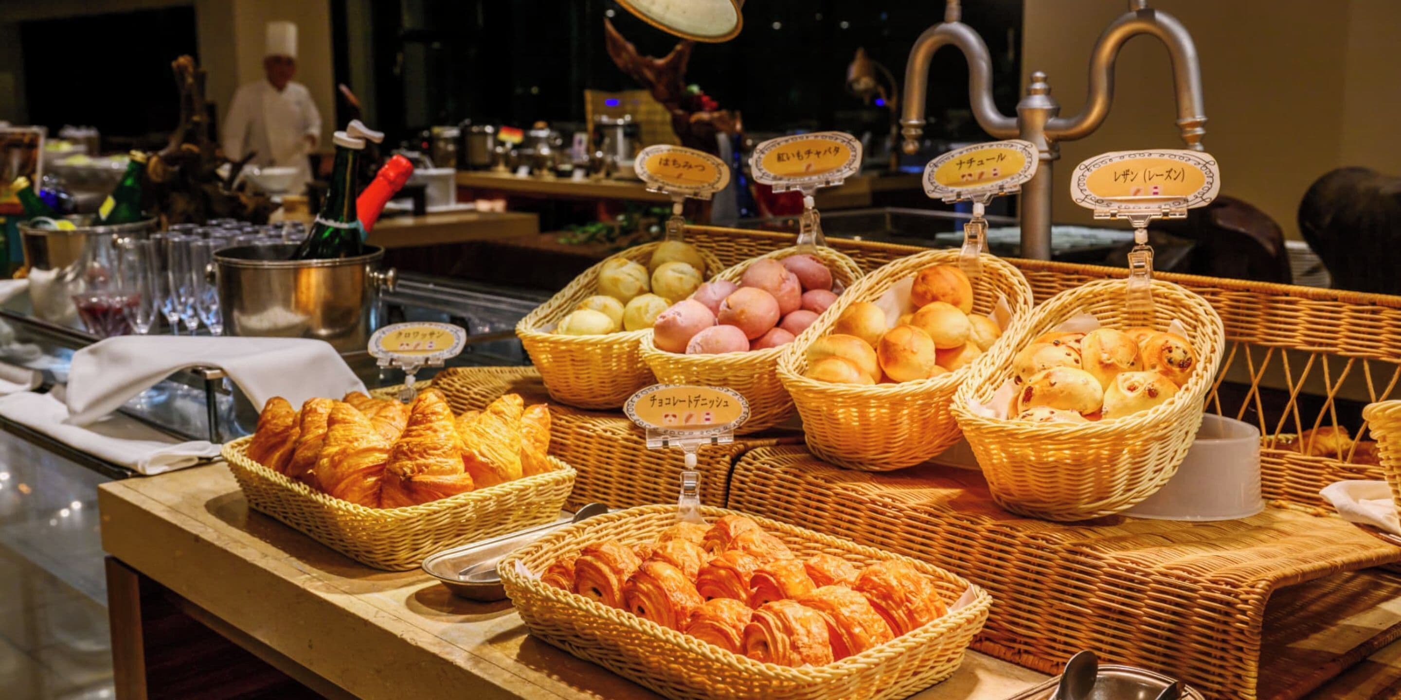A buffet with various food items in wicker baskets, including croissants and bread.