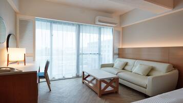 Une chambre d’hôtel équipée d’un canapé, d’une petite table, d’une chaise, d’un bureau avec une lampe et d’un appareil de climatisation.