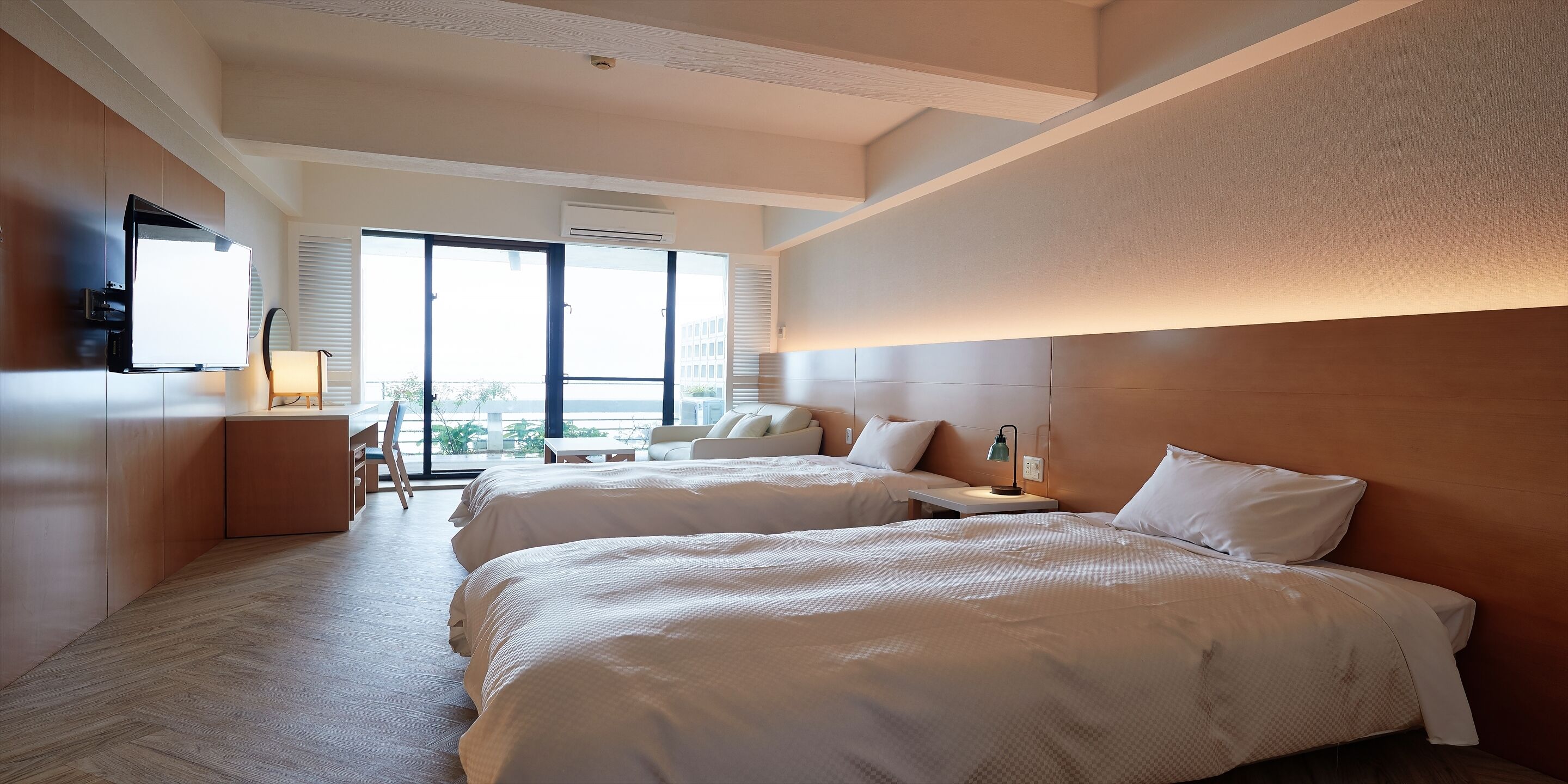 Ein Hotelzimmer mit zwei Betten, einem Schreibtisch, einem Stuhl und einem großen Fenster mit Blick.