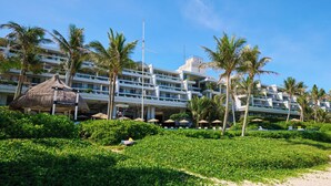 A hotel with multiple floors, palm trees, and a beach area with umbrellas. - Palace in Moon Beach (Onna)