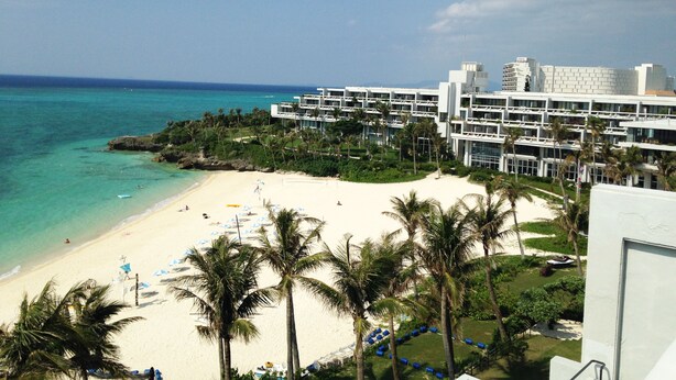 A beachfront hotel with multiple floors, a sandy beach, and palm trees. - Palace in Moon Beach (Onna)