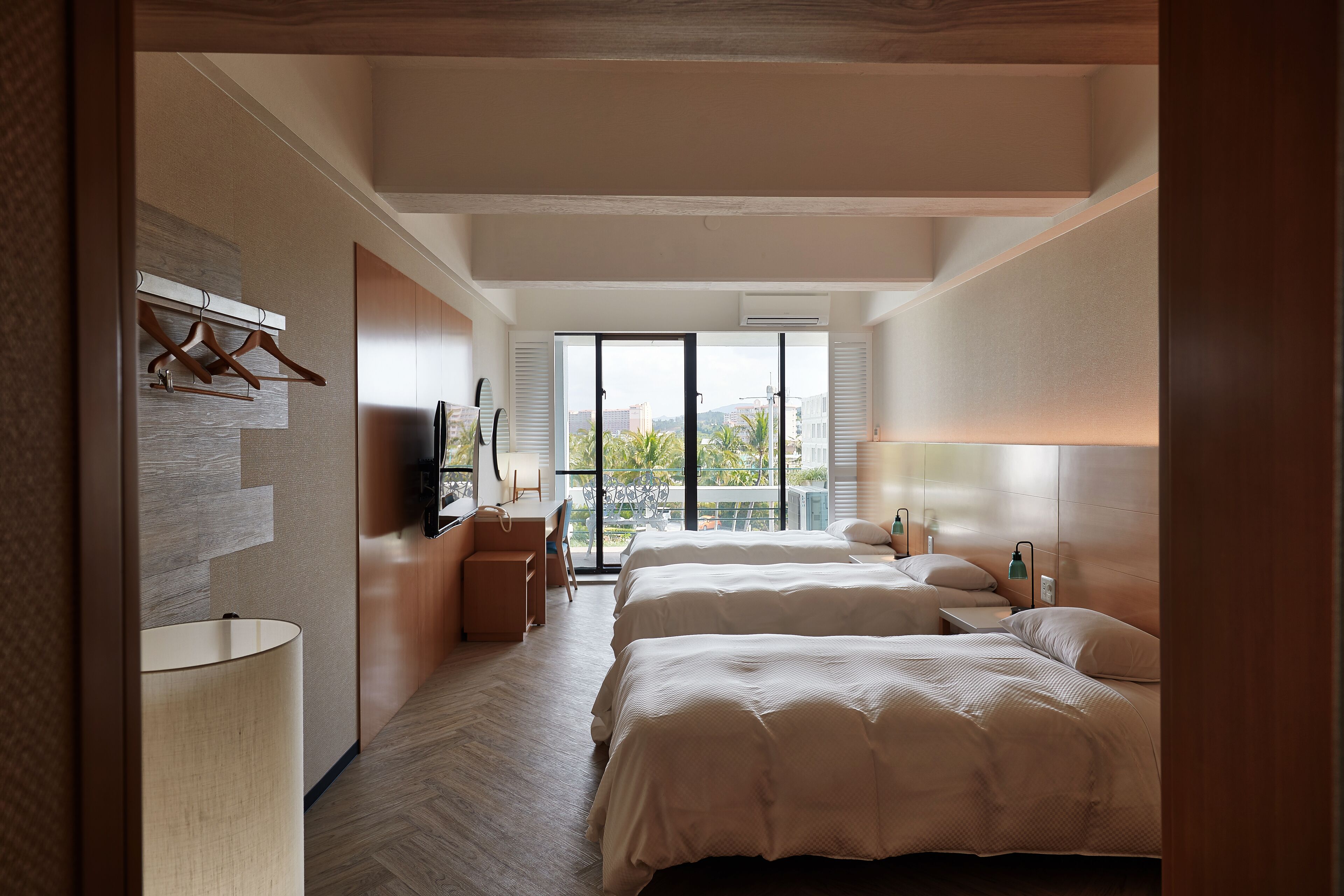 A modern hotel room with two beds, a desk, and a balcony with a view.