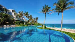 A resort pool with clear blue water, surrounded by palm trees and a beach view. - Palace in Moon Beach (Onna)