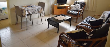 A living room with a dining table, chairs, a sofa, a TV, and a fan.