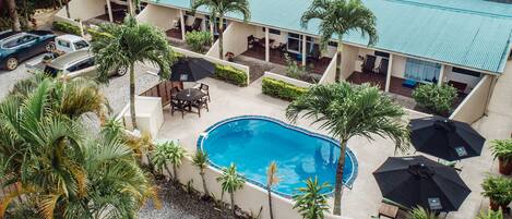 Un área de piscina en la azotea con una piscina azul, rodeada de palmeras y mobiliario exterior.