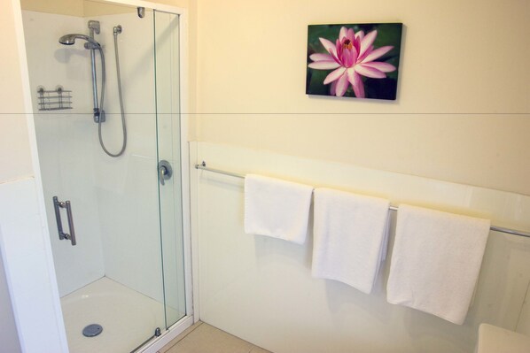Un baño moderno con cabina de ducha de vidrio, un perchero blanco y un cuadro de flores en la pared.
