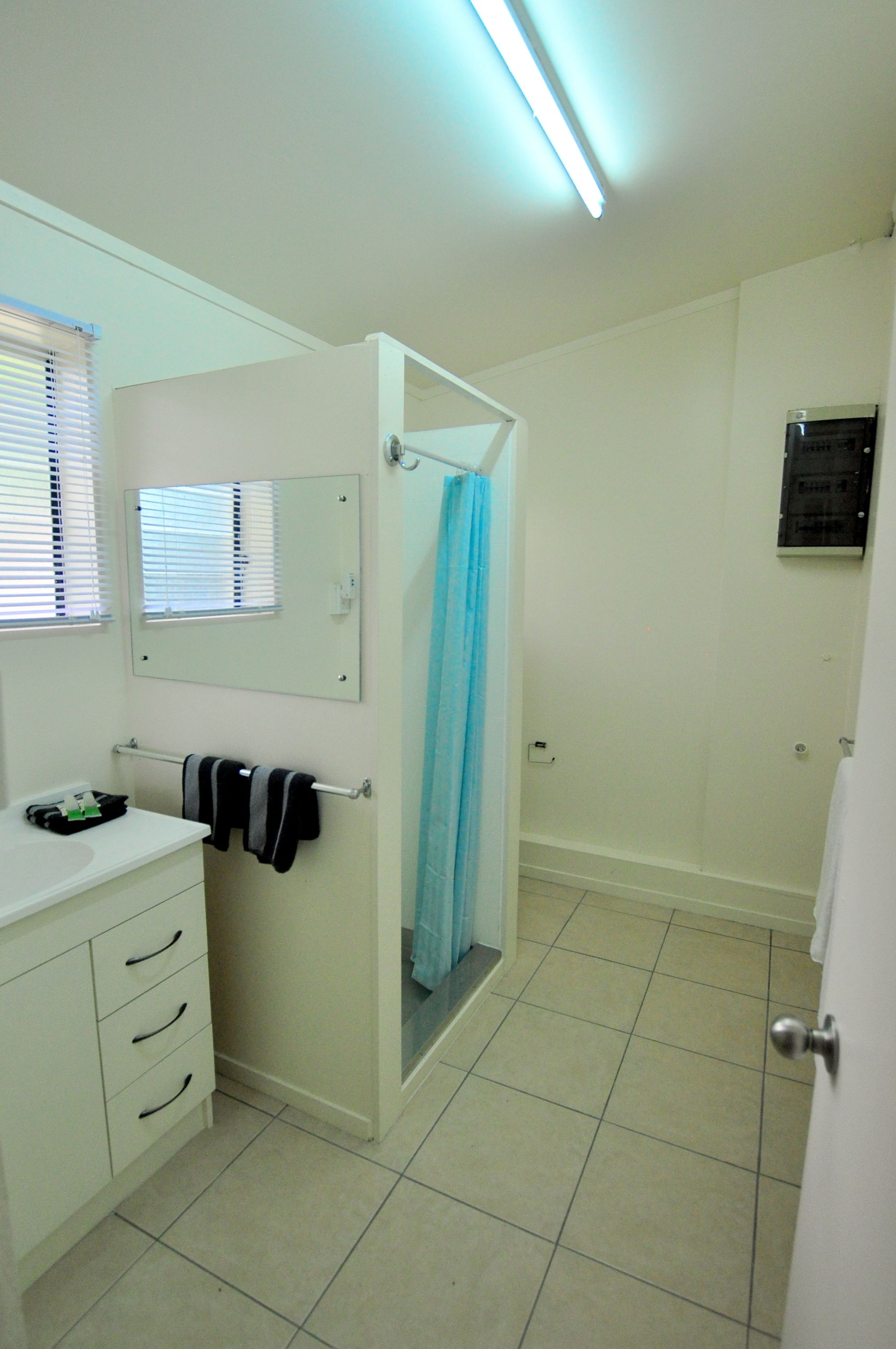 A bathroom with a white vanity, a towel rack with towels, a mirror, a shower with a blue curtain, and a tiled floor.