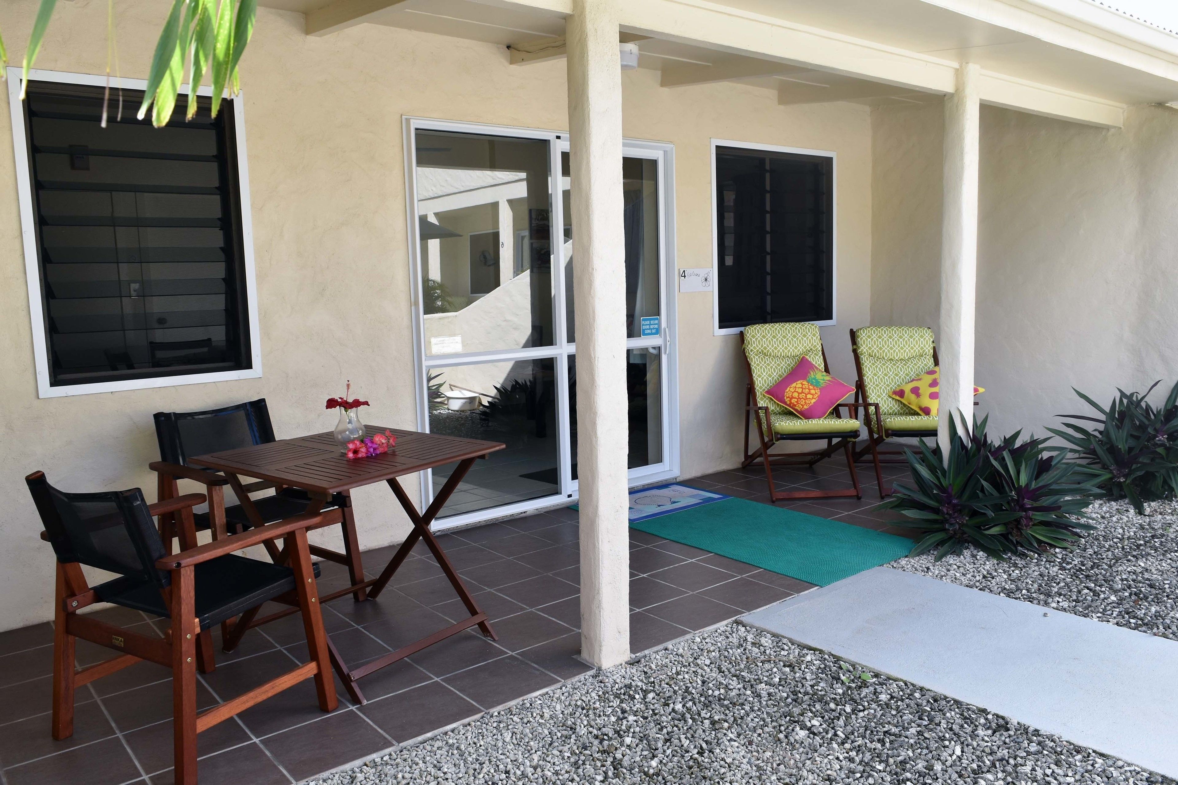 An outdoor patio area with a wooden table and chairs, a small plant, and a tiled floor.