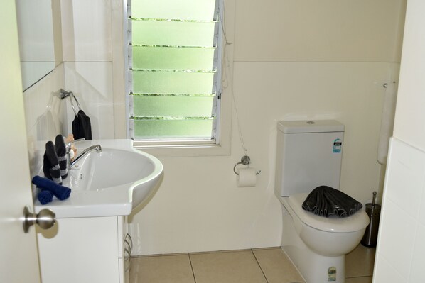 A small, clean bathroom with a white sink, toilet, and window with blinds.