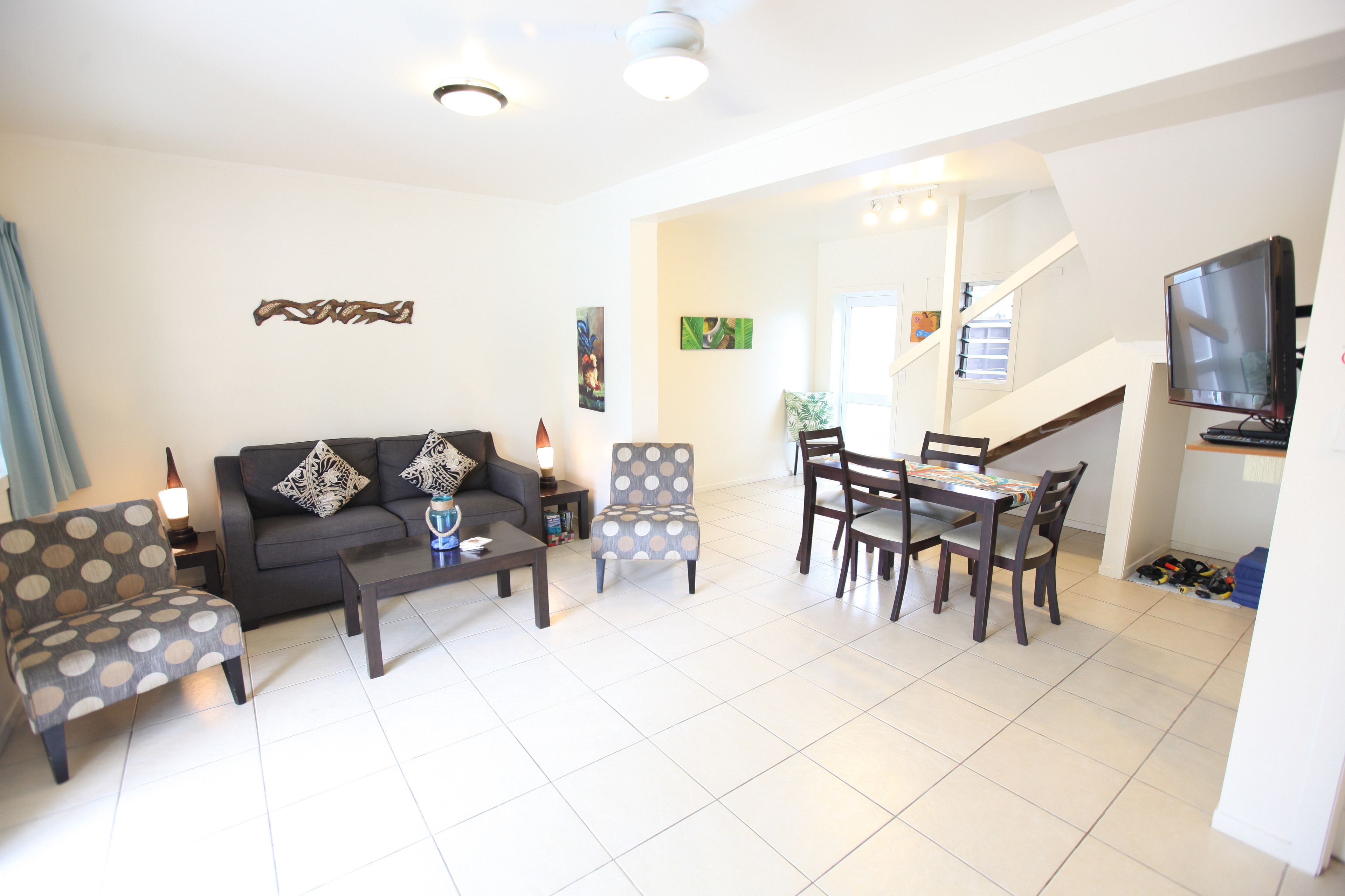 Un salon comprenant un canapé, des fauteuils, une table basse, une table à manger avec des chaises, un téléviseur et un escalier menant à un autre niveau.
