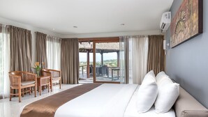 Une chambre d’hôtel dotée d’un grand lit, d’un coin salon avec des fauteuils, d’une table à manger et offrant une vue sur l’extérieur grâce à une porte vitrée.