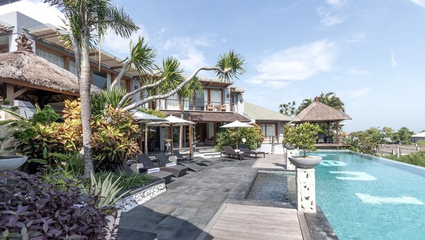 Un complexe hôtelier doté d’une piscine, de chaises longues et de plantes tropicales.