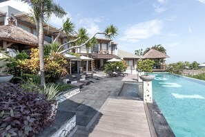 A resort with a pool, lounge chairs, and tropical plants. - Hening Jimbaran (Jimbaran)