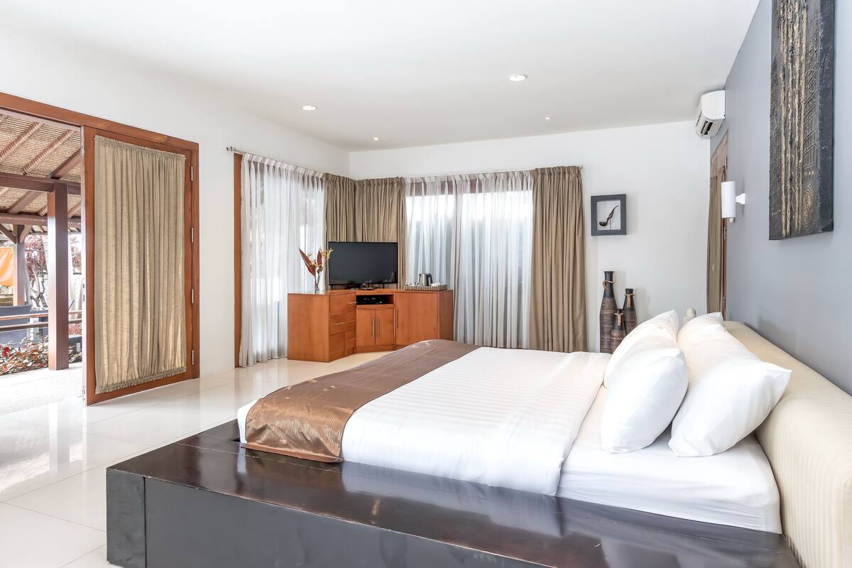 Habitación de hotel moderna con una cama grande, televisión, cómoda de madera y balcón.