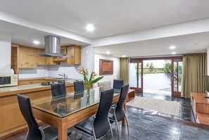 A modern kitchen with a glass dining table, black chairs, and a stainless steel range hood. - Hening Jimbaran (Jimbaran)