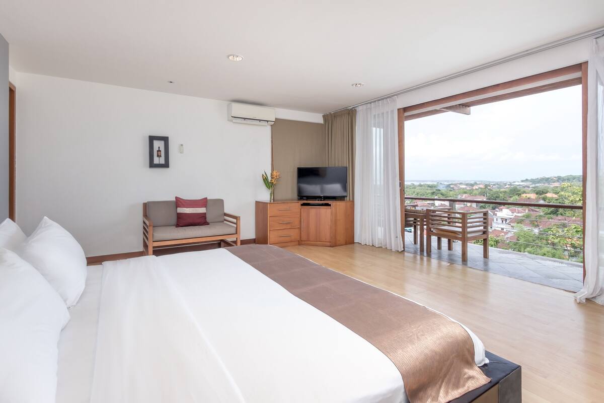 Habitación de hotel con una cama grande, televisión, escritorio con silla y balcón con vistas.