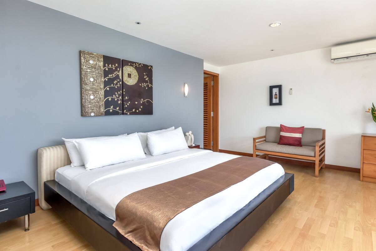 Un dormitorio moderno con una cama grande, una mesita de noche, una silla y una obra de arte colgada en la pared.