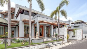 Un bâtiment moderne avec une façade en pierre, des pergolas en bois et des palmiers.