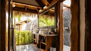 A bathroom with a stone wall, wooden beams, and a sink with two basins. - Aitutaki Escape (Aitutaki)