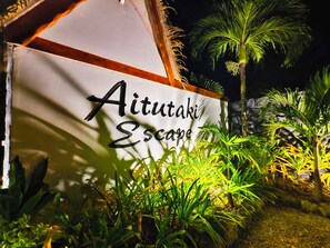 En skylt för ”Aitutaki Escape”, omgiven av tropiska växter.