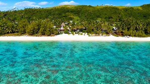 A coastal area with clear turquoise water, a sandy beach, and a forested hill with buildings. - Aitutaki Escape (Aitutaki)