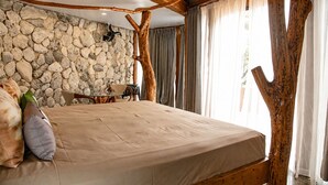 A bedroom with a stone wall, wooden beams, a bed, a table, and a chair. - Aitutaki Escape (Aitutaki)