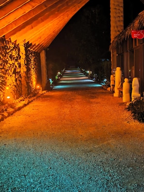 A pathway leading to a building with a thatched roof and stone walls, illuminated by warm lighting.