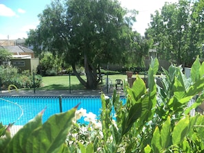 A backyard with a swimming pool, a large tree, and a fenced area with a chair and table.