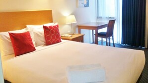 Ein Hotelzimmer mit einem großen Bett, zwei roten Kissen, einem Holz-Kopfteil, einem Nachttisch mit einer Lampe, einem Schreibtisch und einem Stuhl.