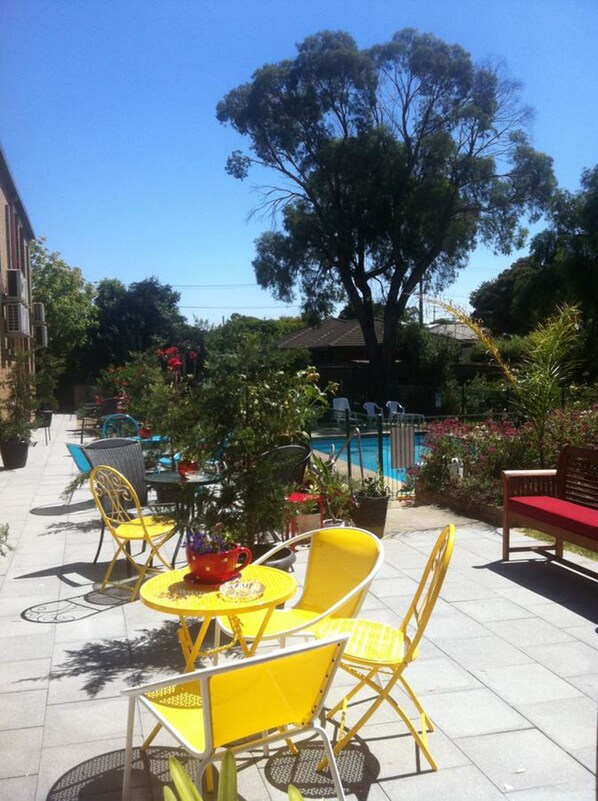 An outdoor patio area with yellow chairs and tables, a pool, and a large tree.