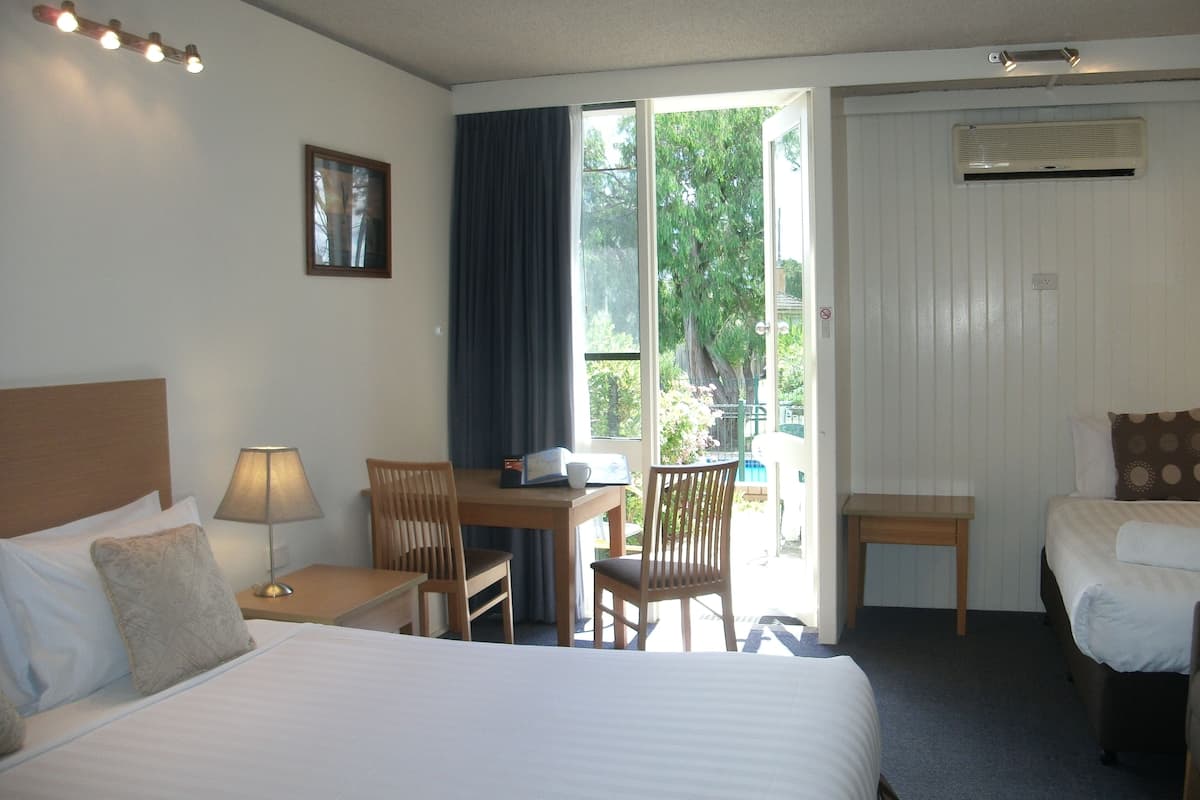 A hotel room with a large bed, a desk with a chair, a small table, a window with curtains, and a ceiling light fixture.