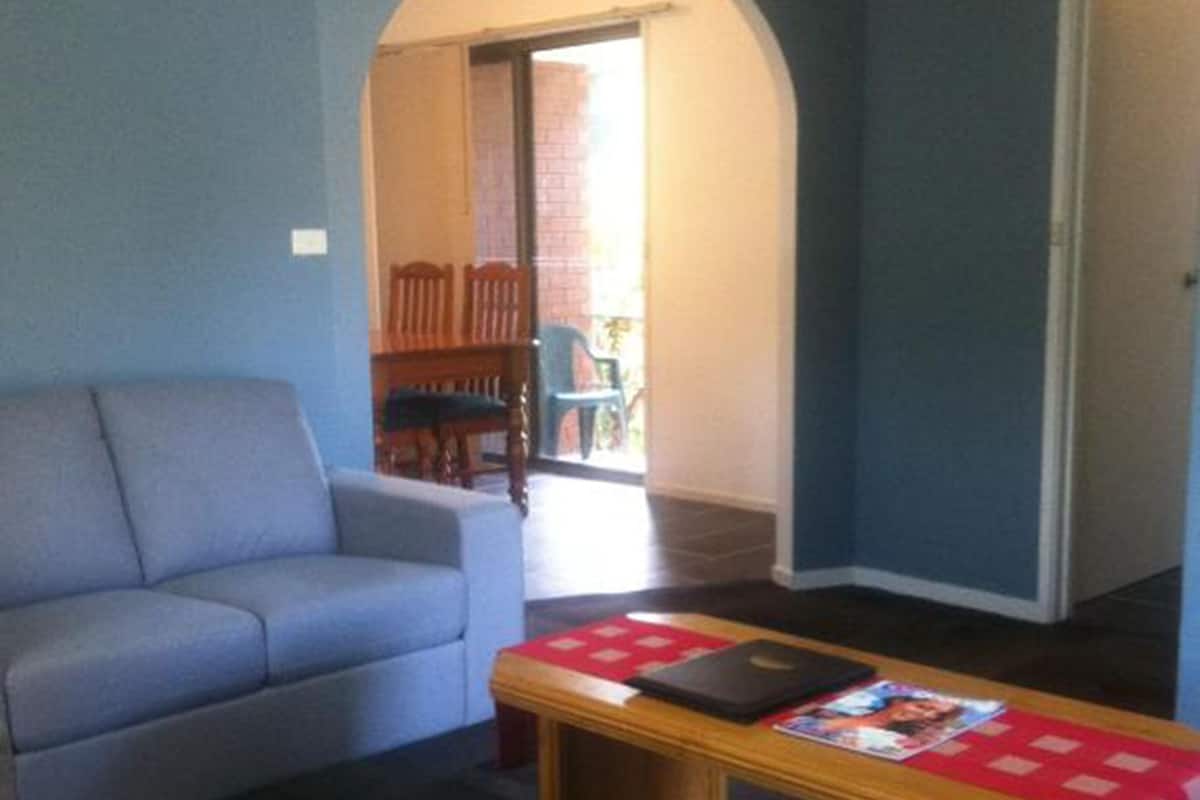 A living room with a blue sofa, a wooden coffee table with magazines, and a door leading to a balcony.