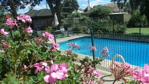 Ein Swimmingpool, umgeben von einem grünen Zaun, mit rosafarbenen Blumen im Vordergrund.