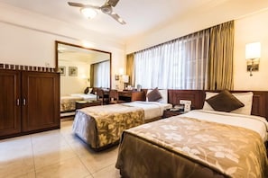 A hotel room with two beds, a desk, a chair, a wardrobe, and a ceiling fan.