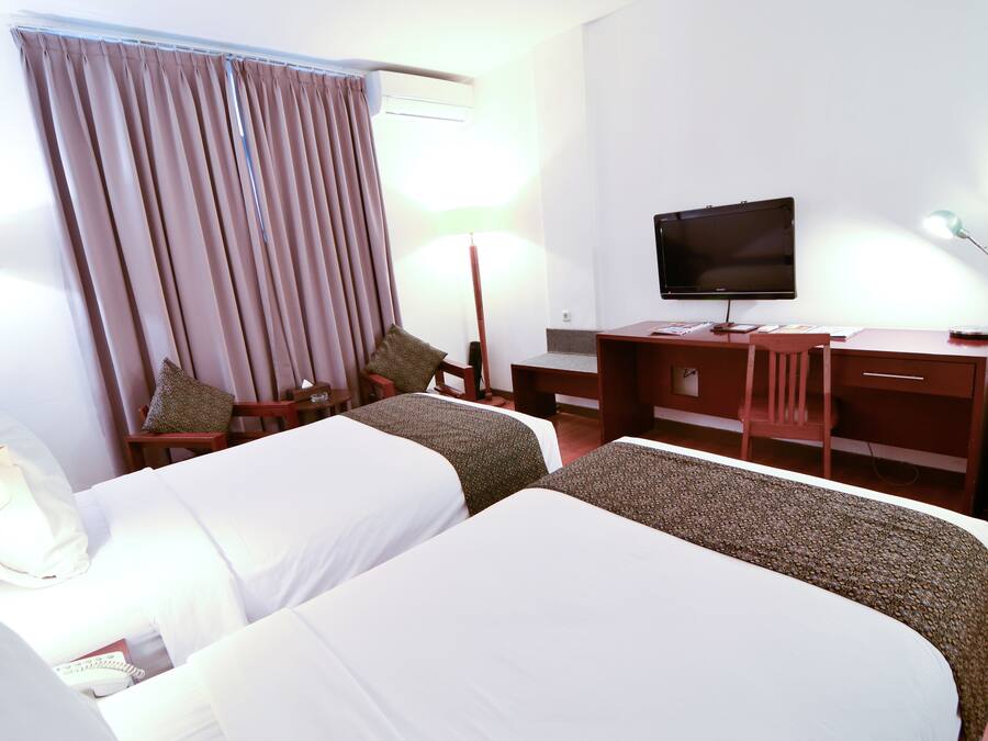 Habitación de hotel con dos camas, un escritorio, una silla, un televisor y una lámpara.