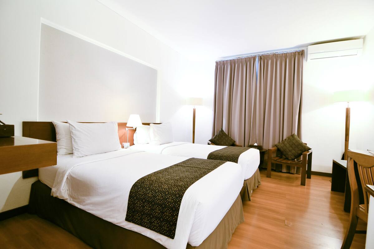 Habitación de hotel con dos camas, un escritorio, una silla y una ventana con cortinas.