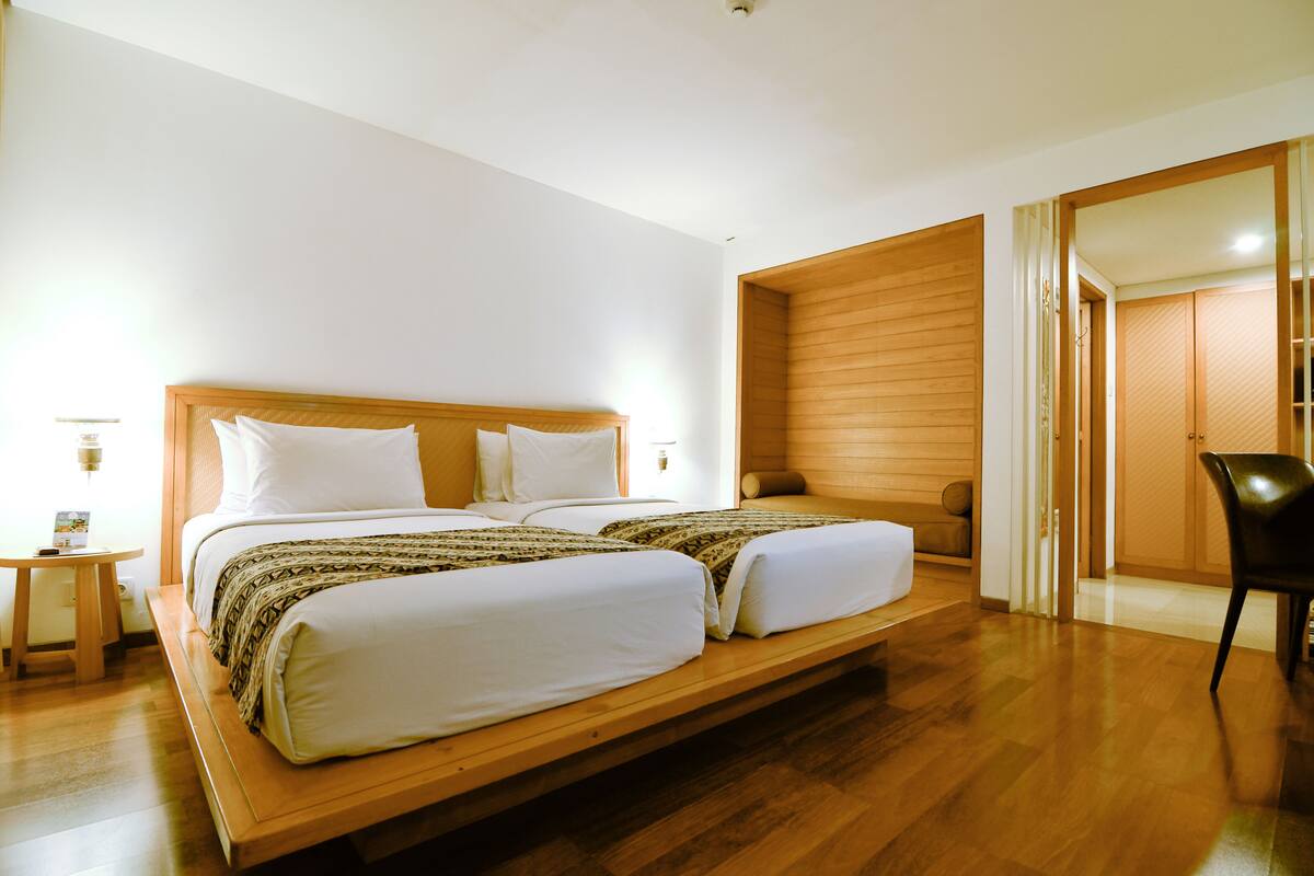 Una cama doble con cabecera de madera, una mesita de noche y una silla en una habitación moderna con suelo de madera y un ventanal grande.