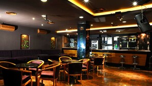 Un área de bar con suelo de madera, taburetes y una barra con dispensador de bebidas.