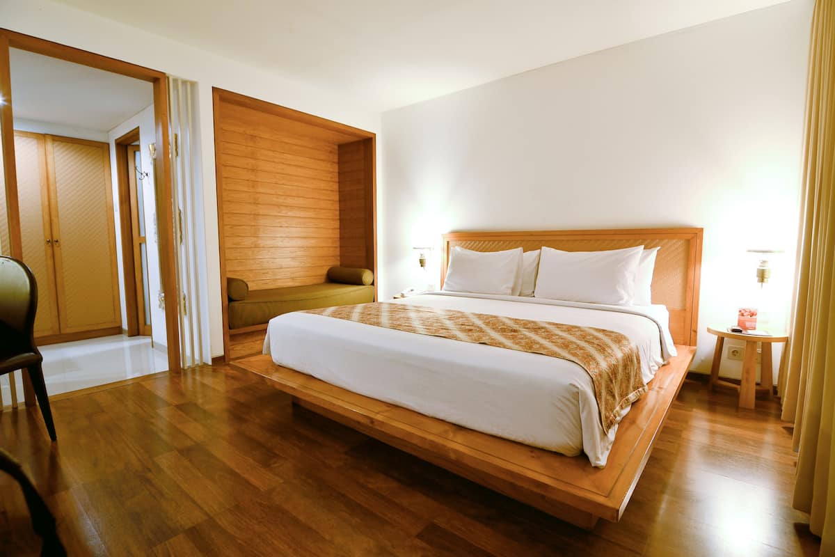 Un dormitorio amplio con una cama grande, suelo de madera, una mesita con lámpara y vistas a una pared de madera y puertas correderas.