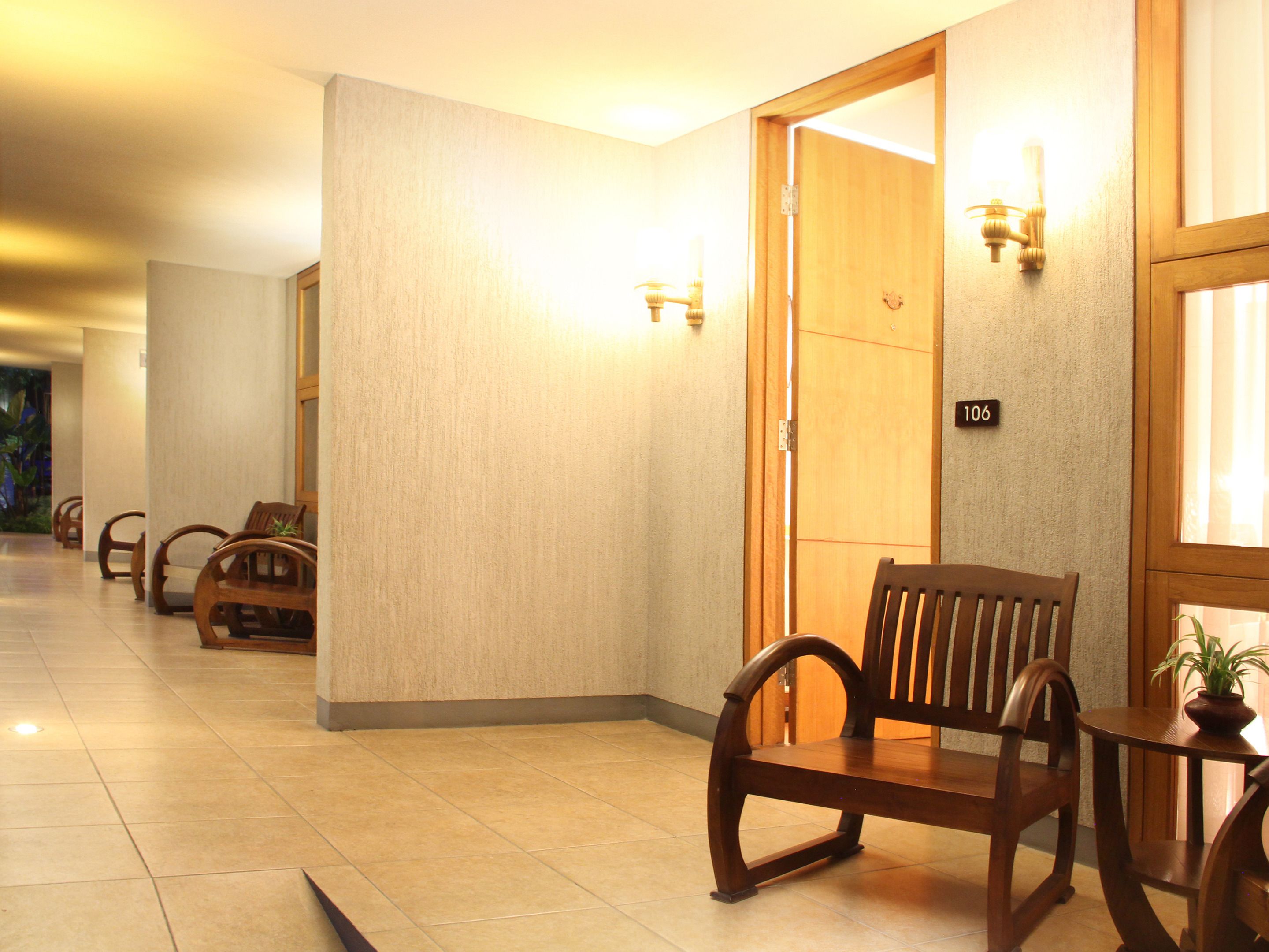 A hotel lobby with wooden chairs, a wooden table, and a door marked with the number 106.