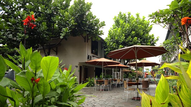 Un patio al aire libre con mesas y sillas, rodeado de exuberante vegetación y flores rojas.