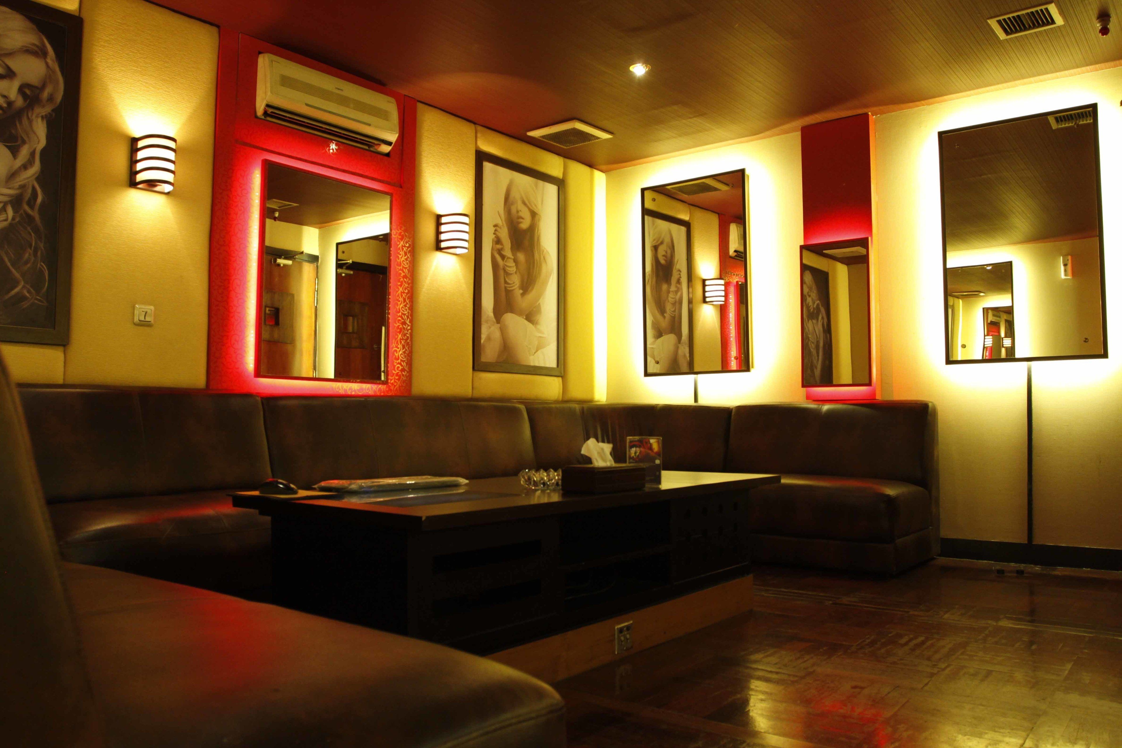A dimly lit lounge area with leather seating, wall-mounted mirrors, and framed pictures.
