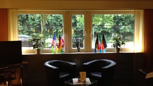A room with two black chairs, a small table with a menu, and a TV on a stand. Flags are displayed on the windowsill. - City Hotel Essen (Essen)